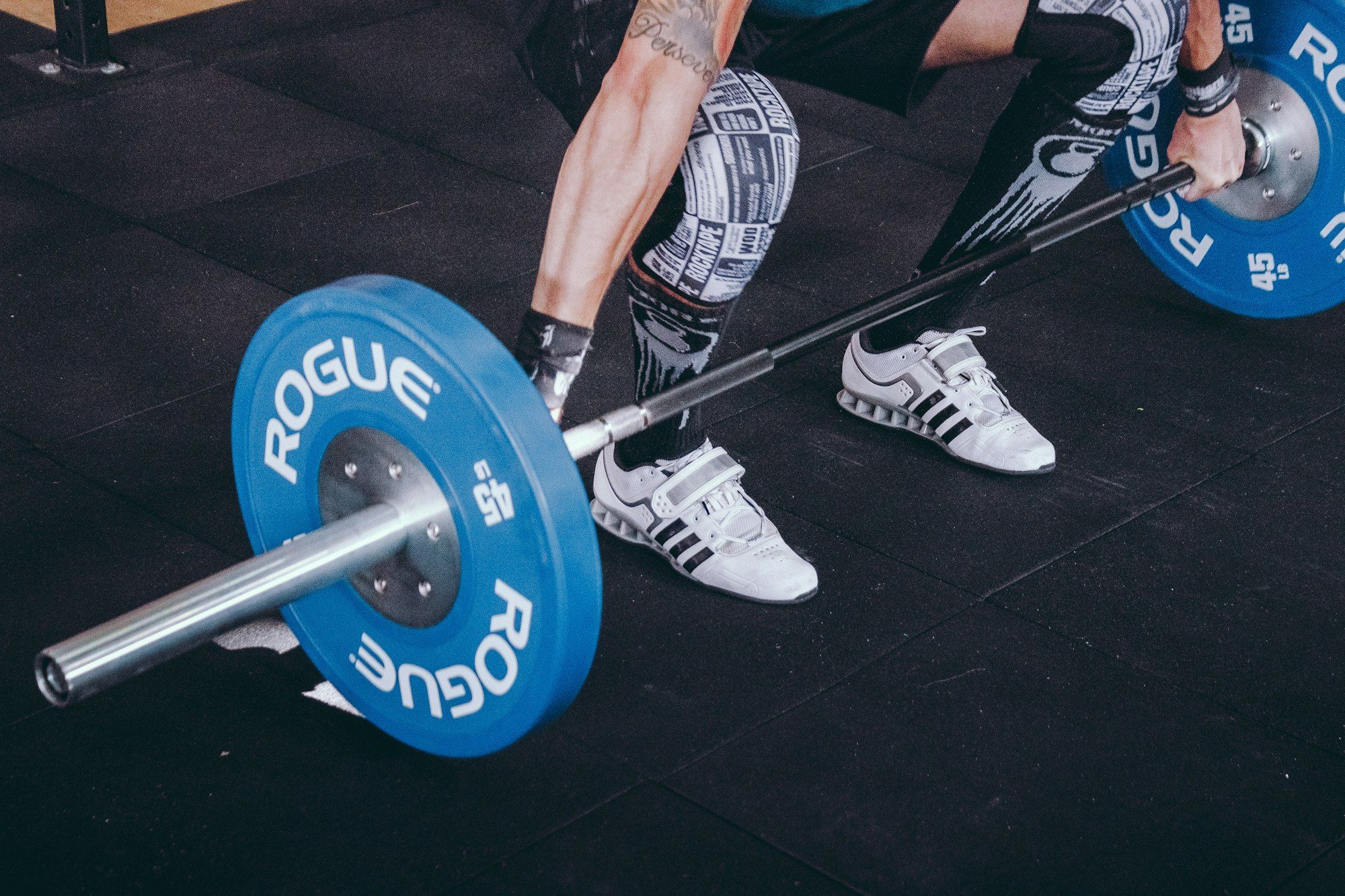 Treino de força em academia, com barra e anilhas sobre piso emborrachado